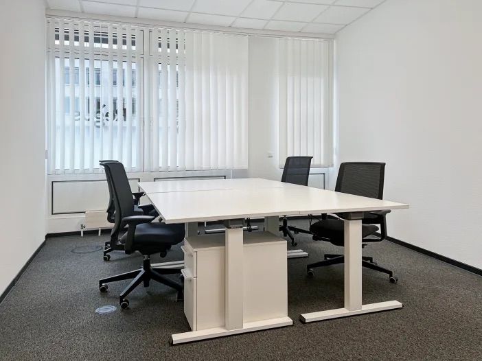 Heller Arbeitsraum mit Schreibtischen, Bürostühlen und großen Fenstern