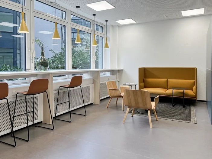 Moderner Wartebereich mit Sitzbank, Stehtischen, Sesseln und großer Fensterfront